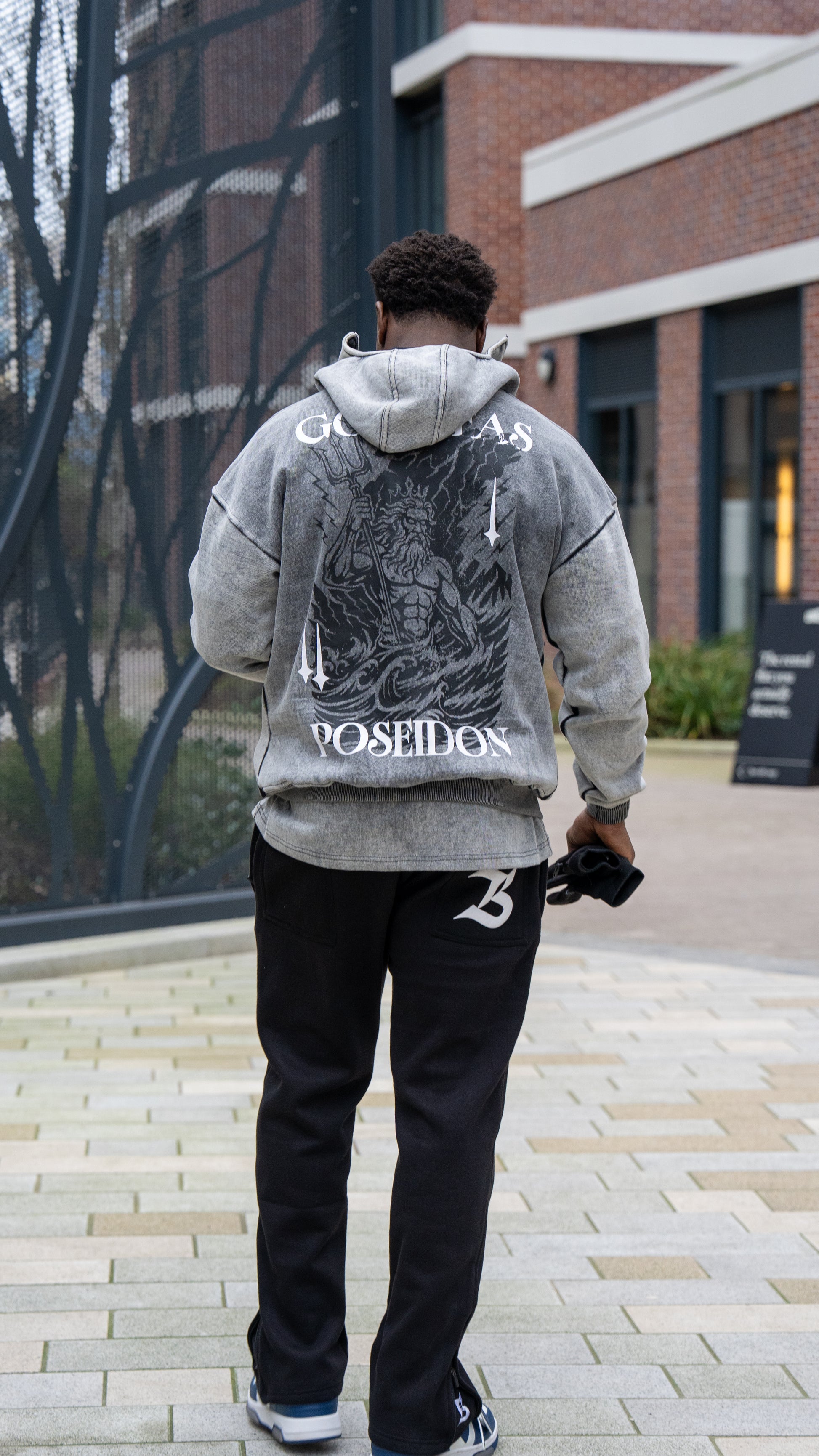Person wearing a gray hoodie with a graphic design, walking outdoors.