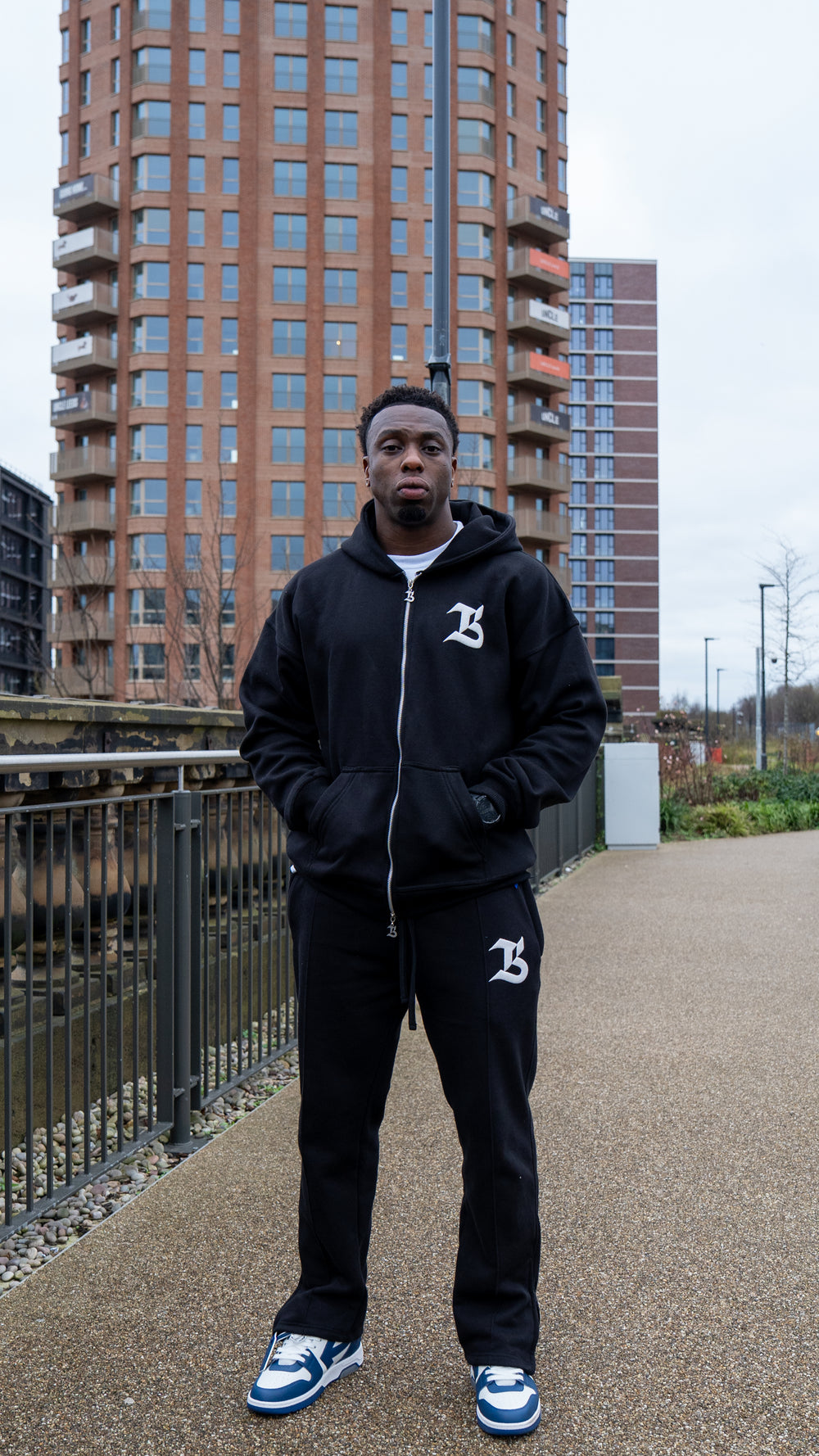Person wearing a black tracksuit with a logo in an urban setting