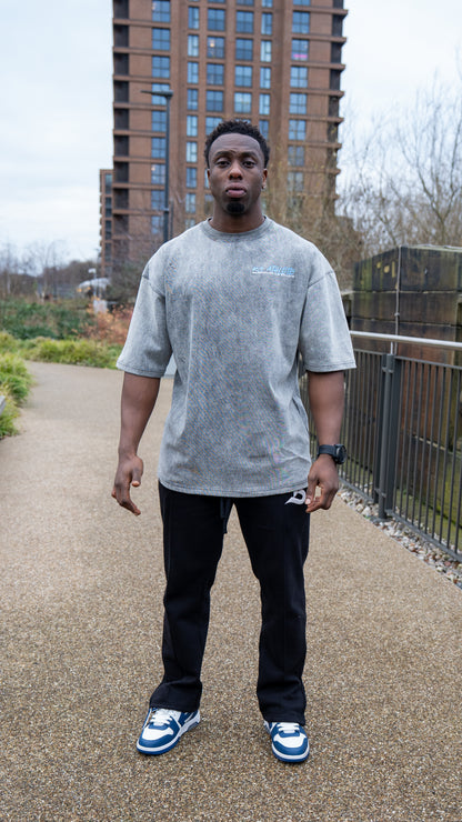 Man wearing a grey t-shirt and black pants standing on a path with buildings in the background