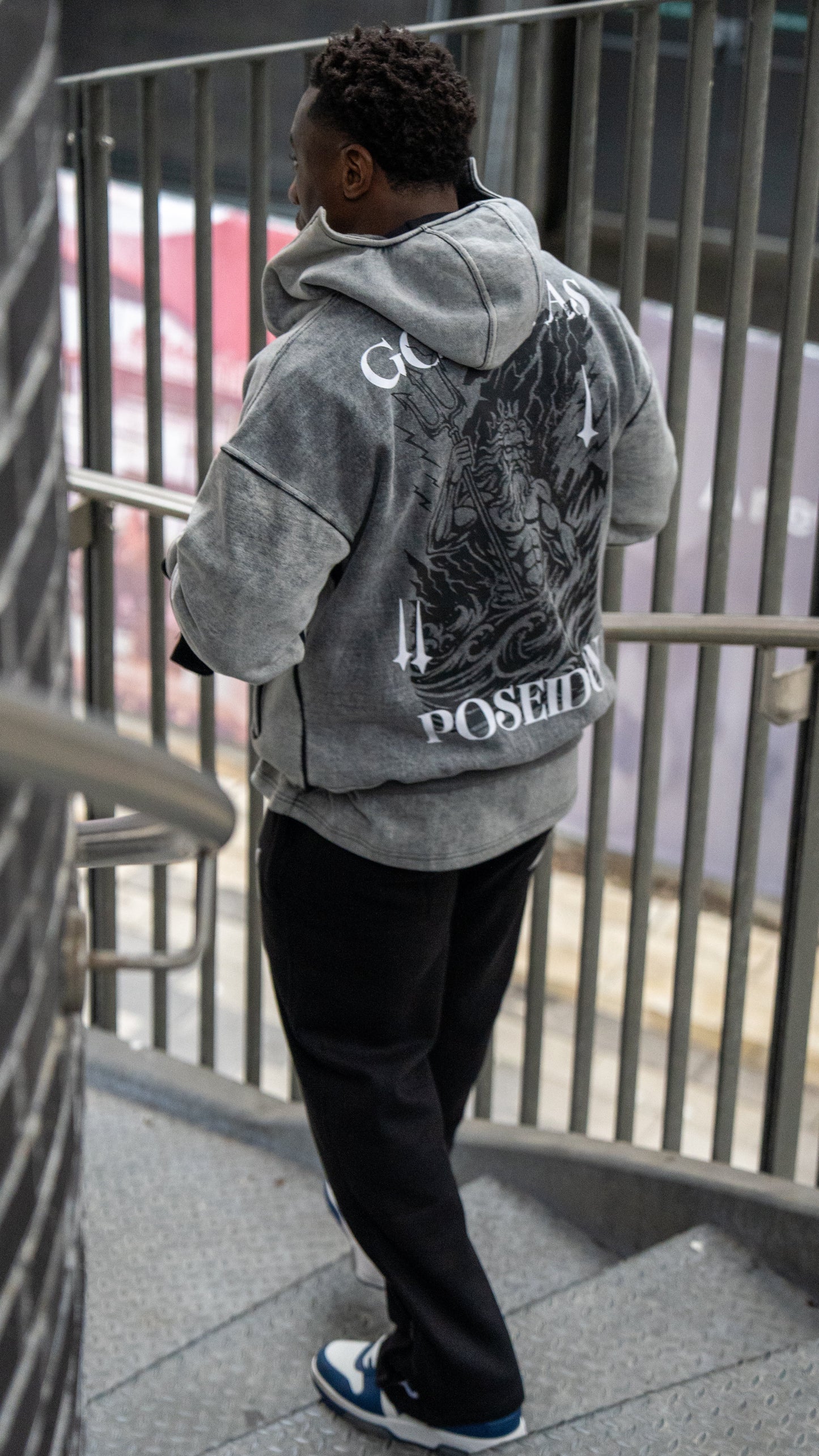 Person wearing a gray hoodie with a graphic design, standing on a staircase.