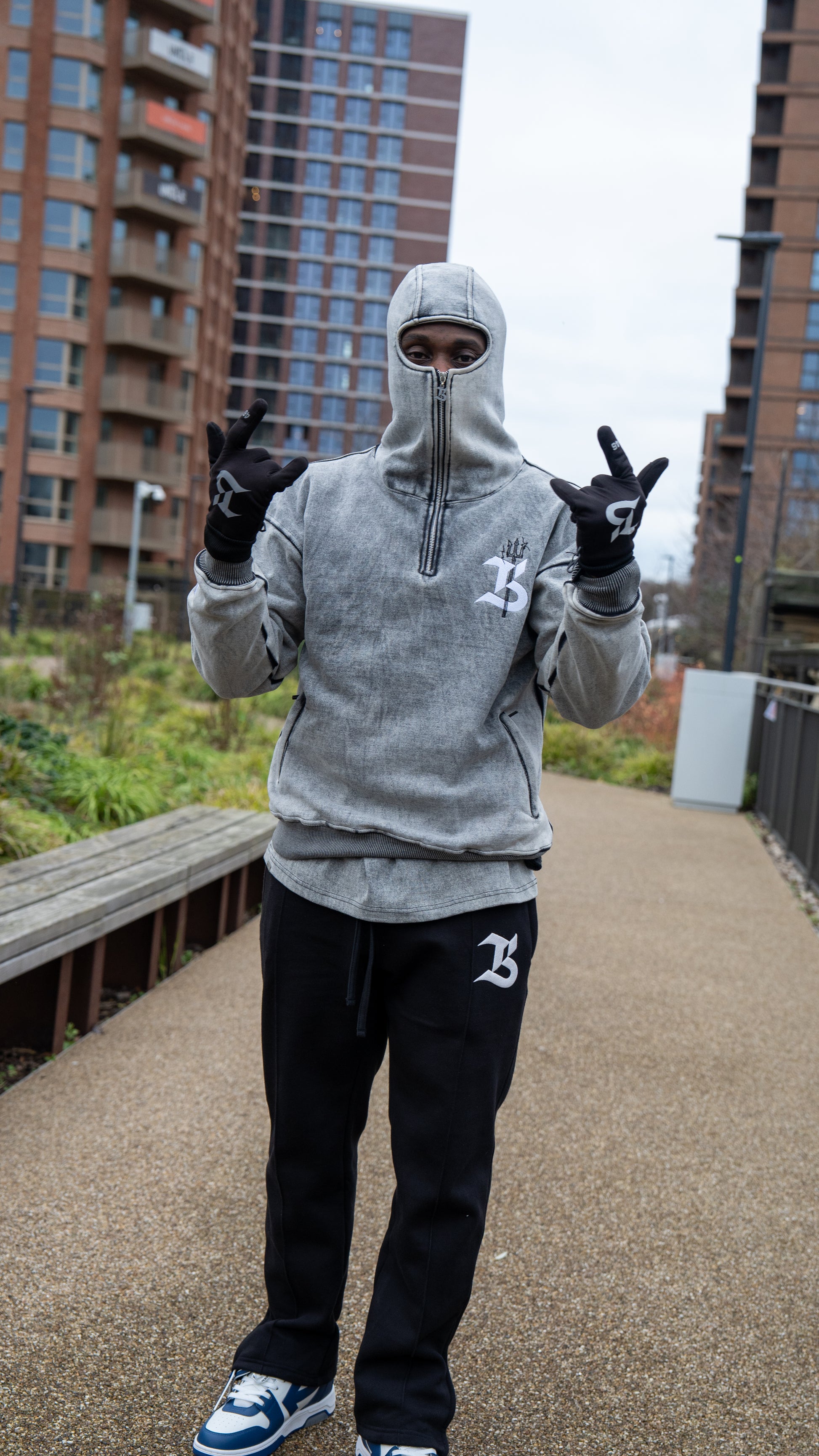 Person wearing a gray hoodie and black pants on an urban pathway with buildings in the background